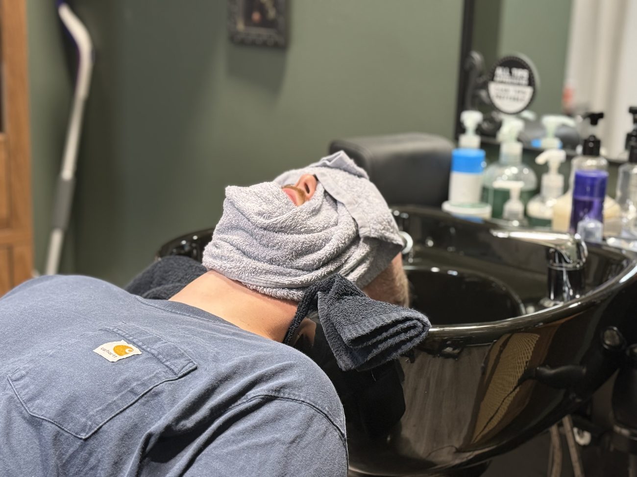 A client reclined at the shampoo bowl with a warm towel folded over his face.